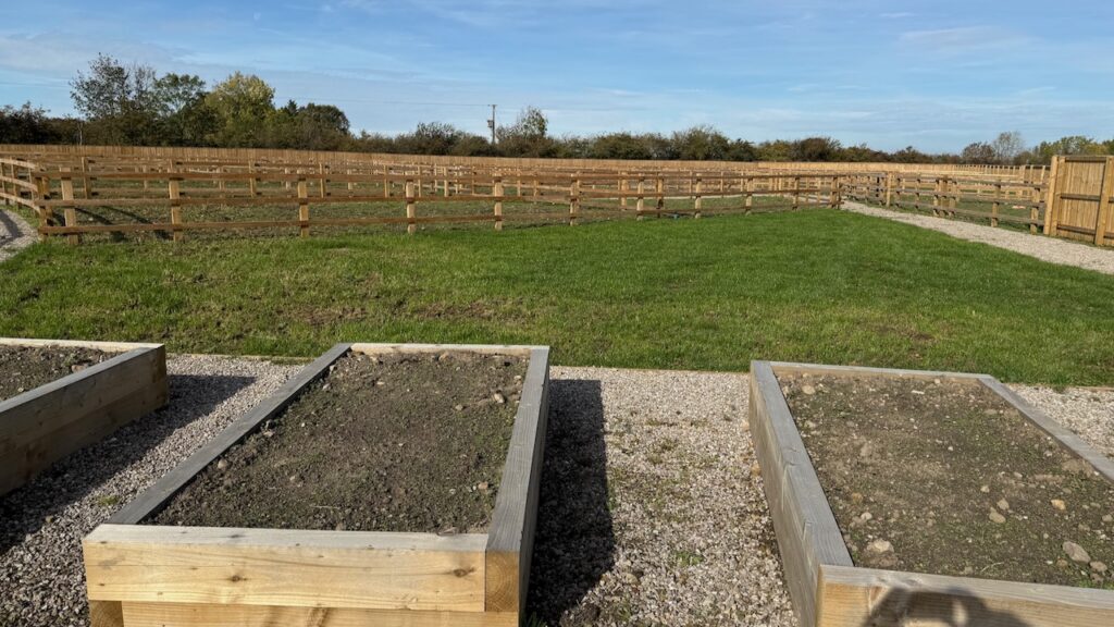 A scene showing raised planters, grass, and fenced areas for the cultivation of crops.